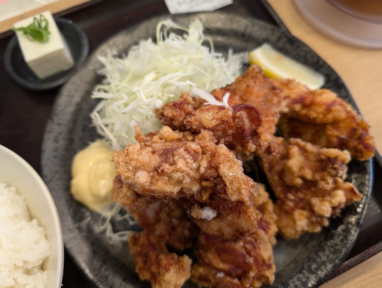 黒い皿に盛られた揚げ物とキャベツ、レモン、豆腐、ご飯