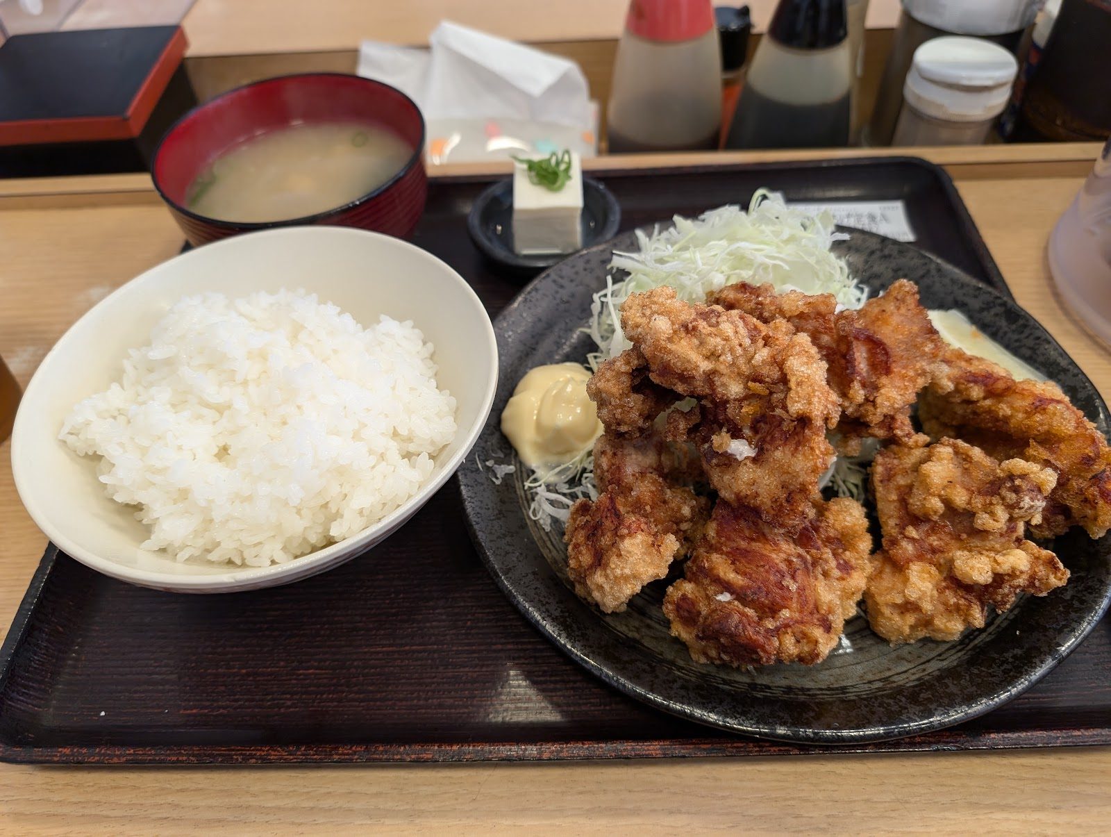 黒い皿に盛られた揚げ物と白ご飯、味噌汁、豆腐が載る定食