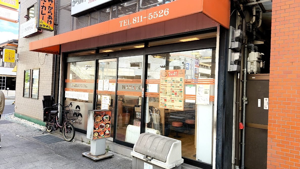 オレンジ色の外壁と大きなガラス窓がある店舗の入口。自転車が停まっている。