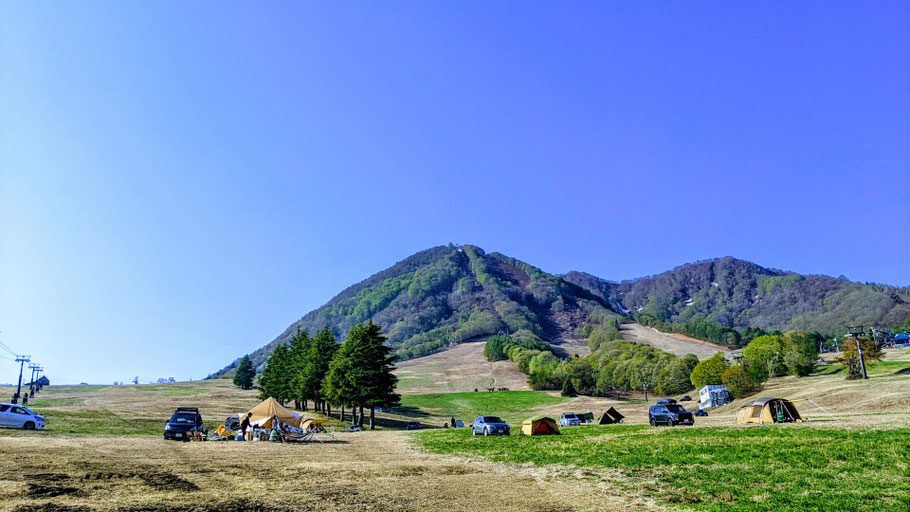 山並みと緑の丘陵が広がる風景、車やテントが点在する