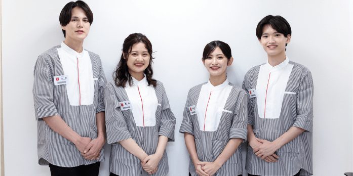 白い壁の前で並ぶ、制服姿の男女4人のスタッフ