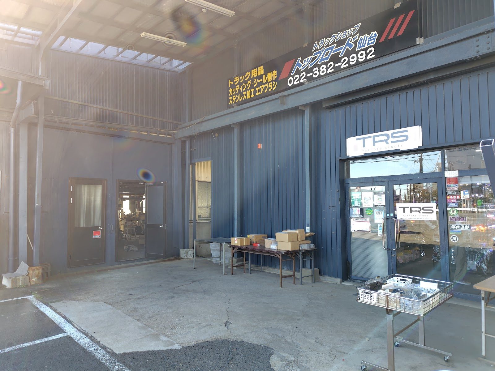 青い外壁の店舗入口と看板、荷物が置かれた手前のスペース
