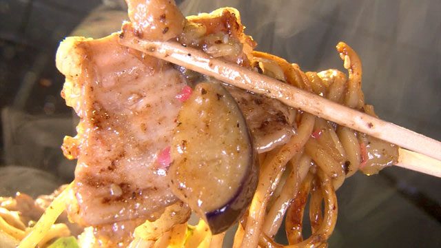 鉄板の上で焼かれるお好み焼きにソースとマヨネーズをかけた様子
