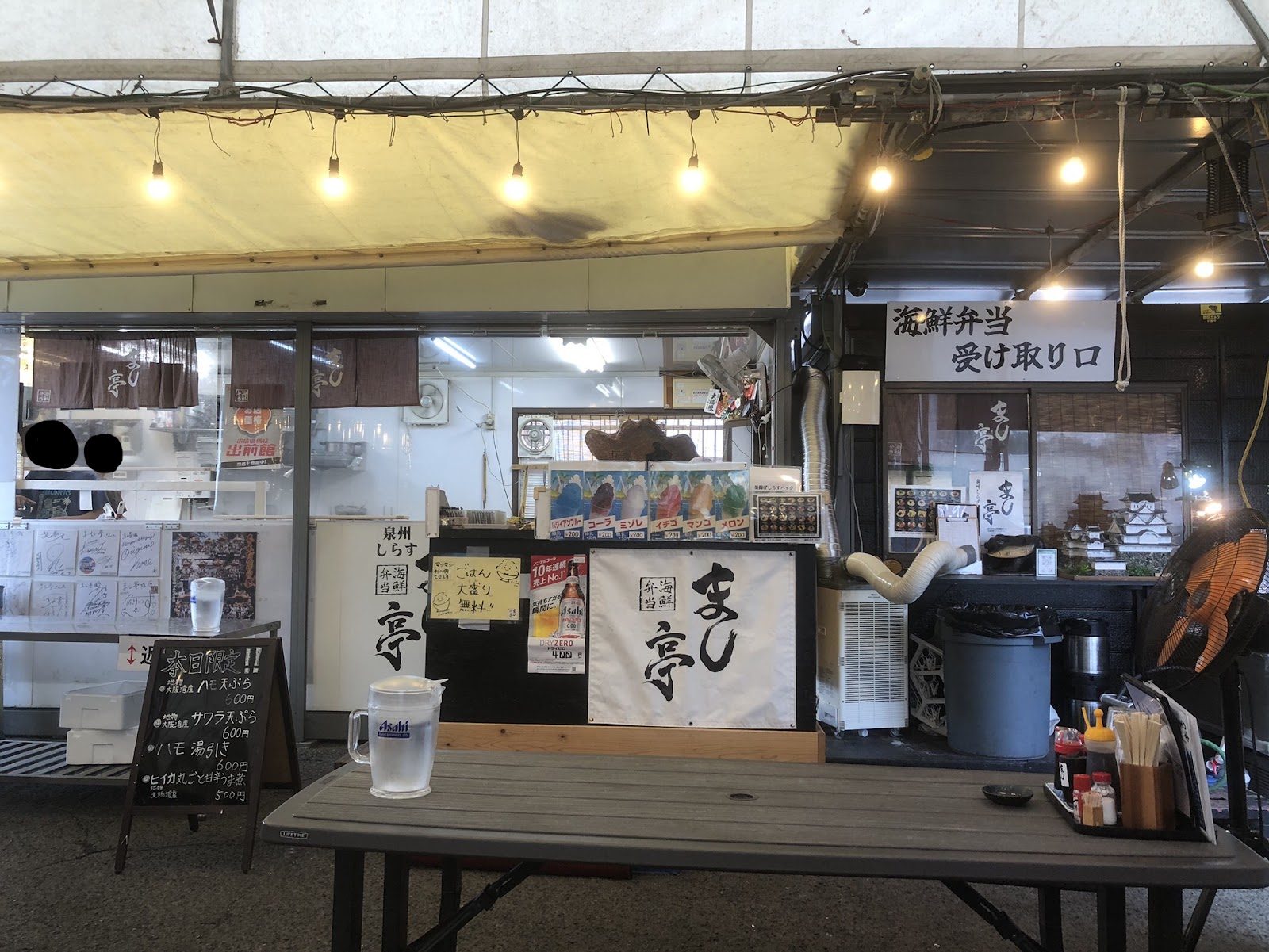 のれんや看板、テーブルが置かれた海鮮弁当店の店先。