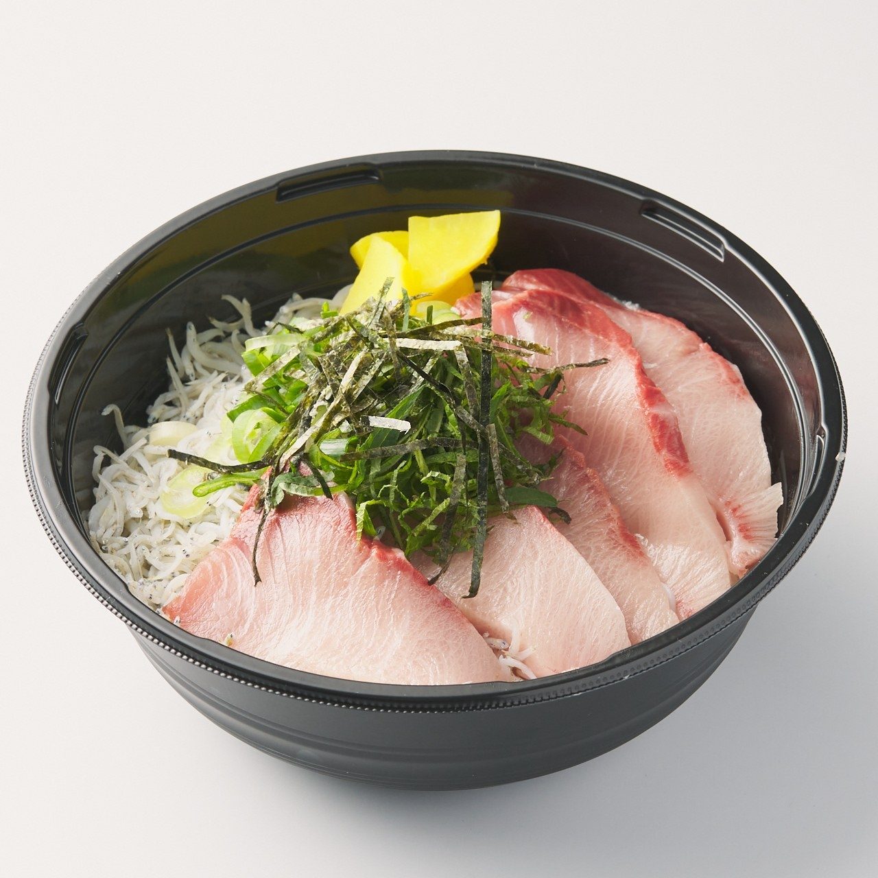 黒い容器に盛り付けられた、切り身の魚と海苔、たくあんの海鮮丼