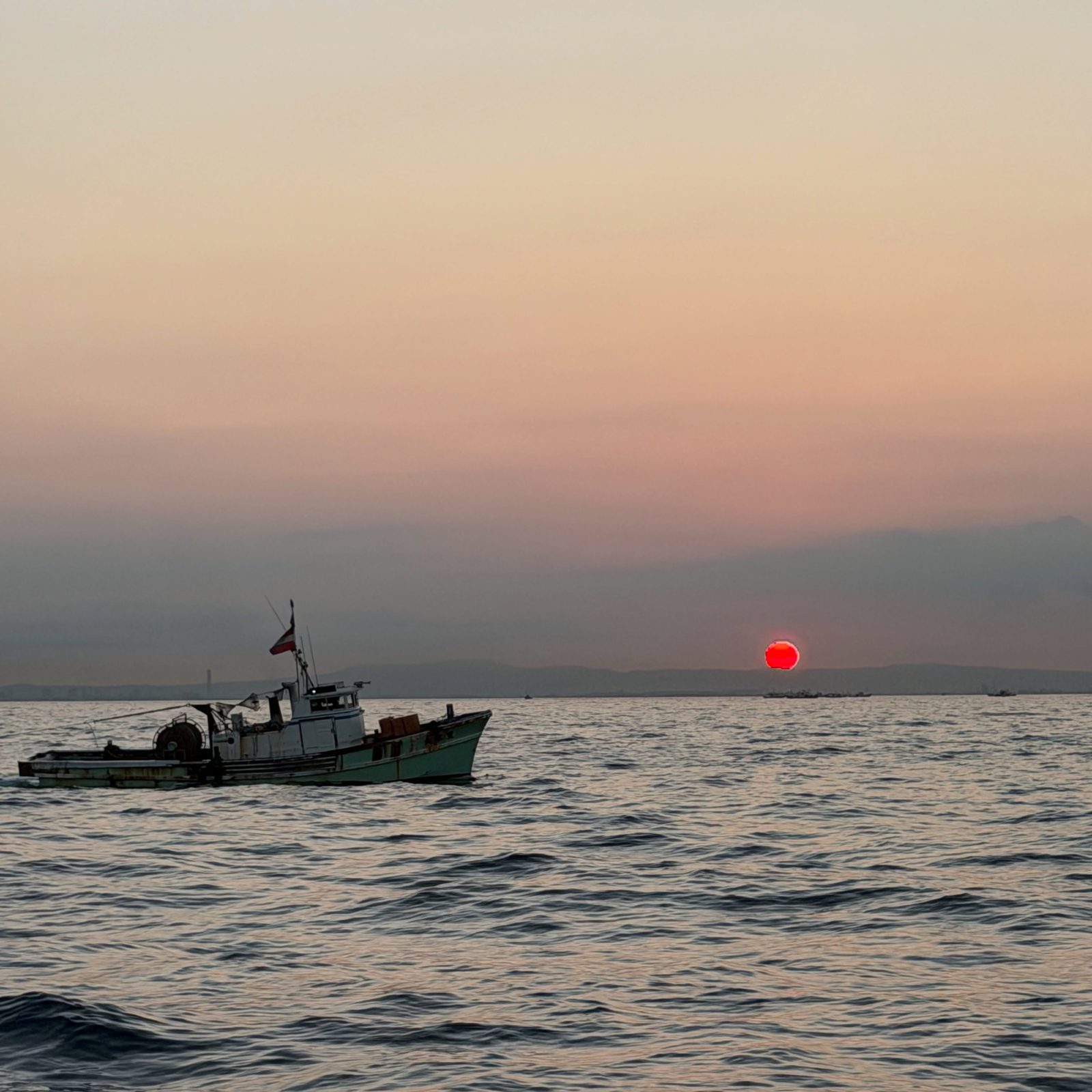 夕日の沈む海に浮かぶ一隻の漁船
