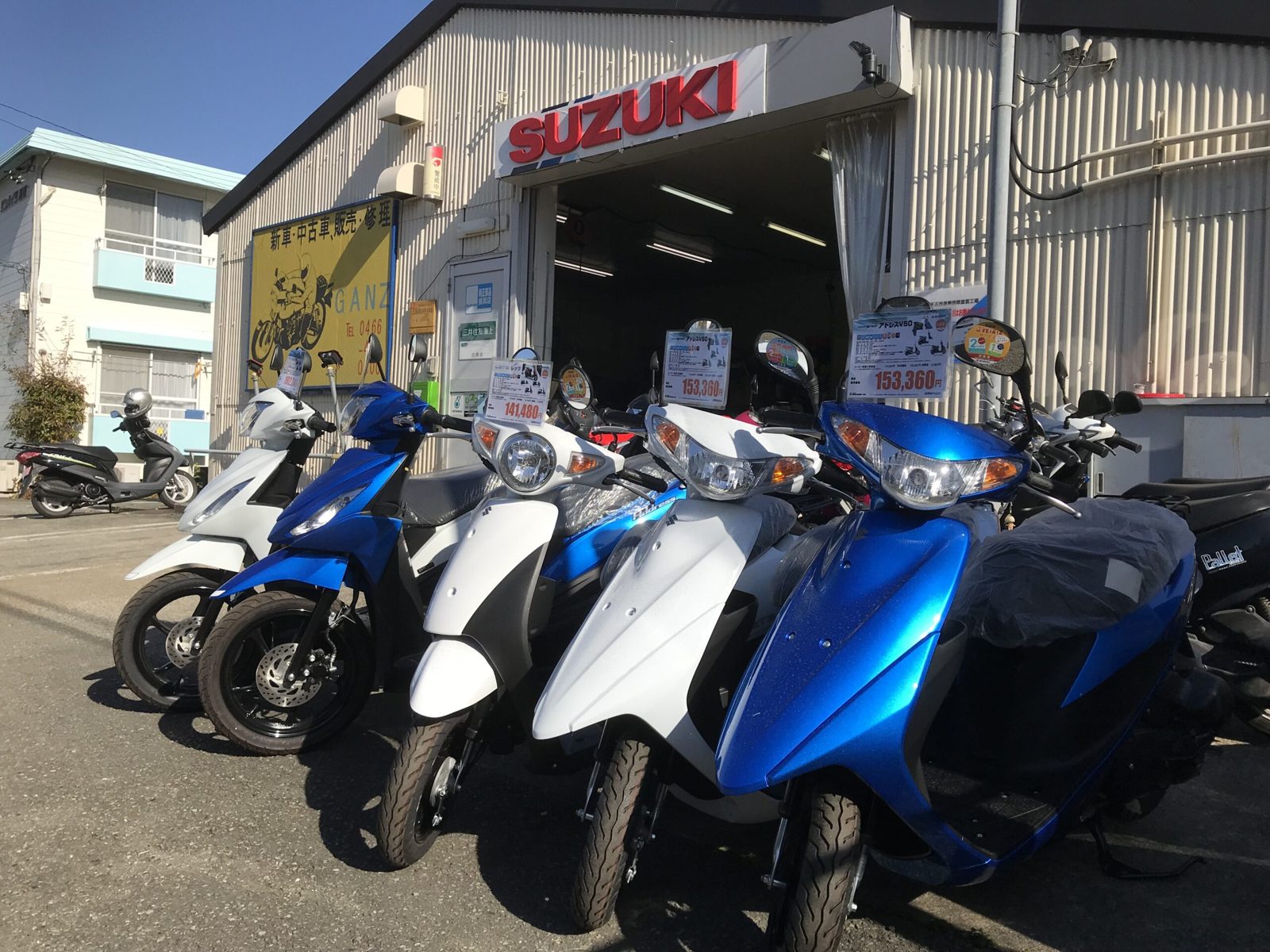 屋外に並ぶ青と白のバイクとSUZUKIの看板