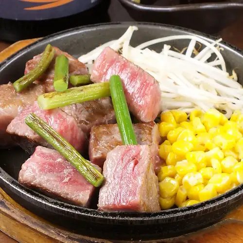 鉄板の上で焼かれる広島焼きにネギと玉ねぎが乗っている