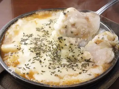 鉄板の上で焼かれる、たっぷりのソースと粉をかけた広島焼き